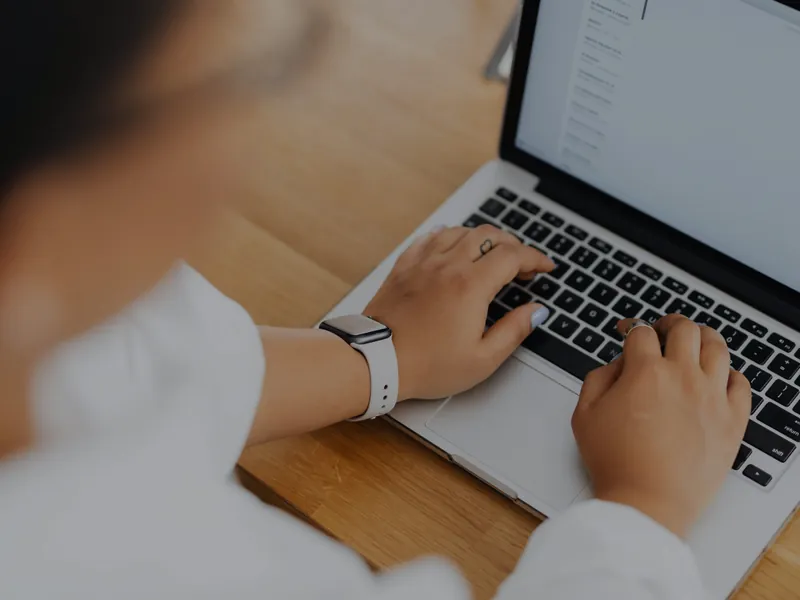 Mâini care tastează la un laptop pe o masă de lemn