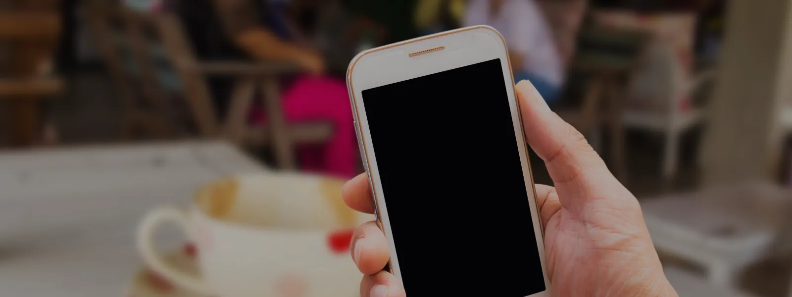 Mână care ține un smartphone într-o cafenea